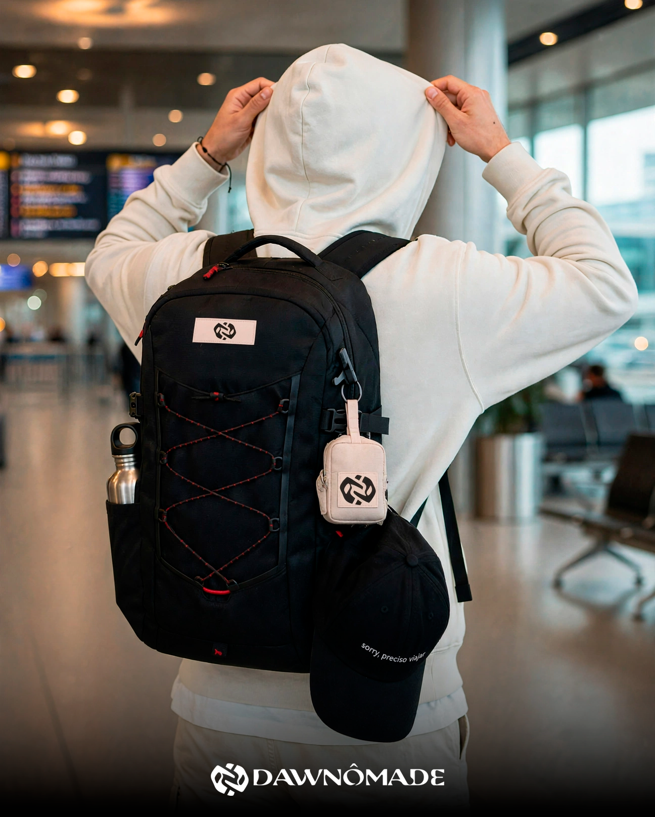 Pessoa de costas em um aeroporto com uma mochila preta DAWNÔMADE e o boné pendurado